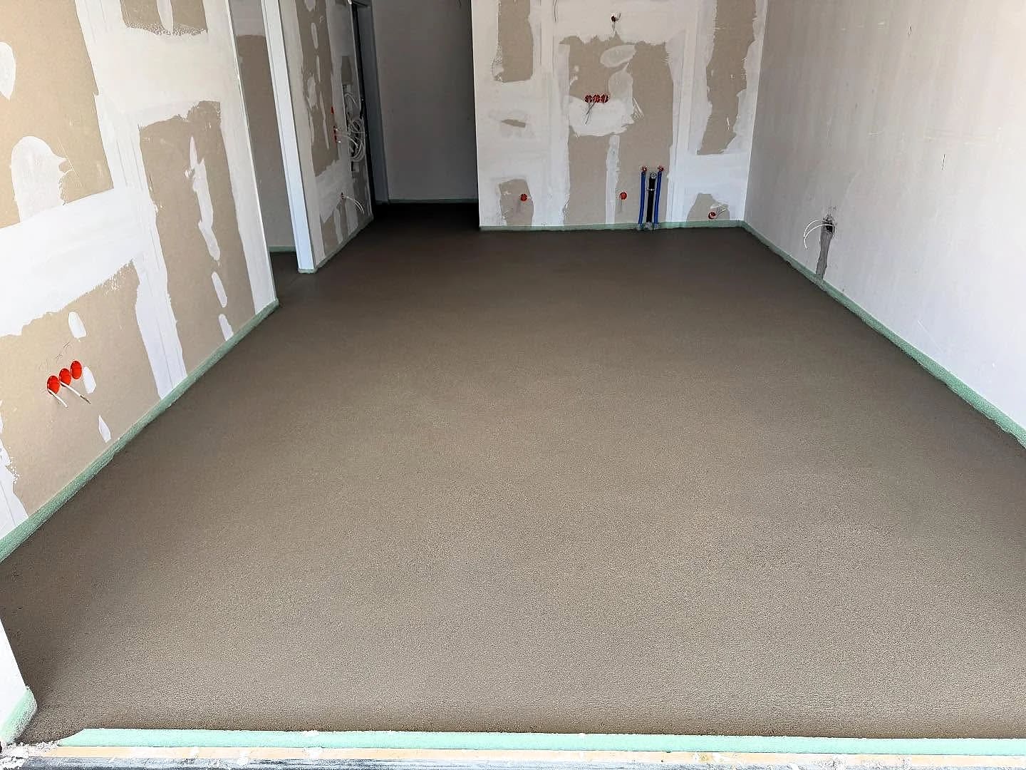 Frisch eingebaute Estrichfläche in einem Wohnraum mit verspachtelten Wänden und grünem Randstreifen